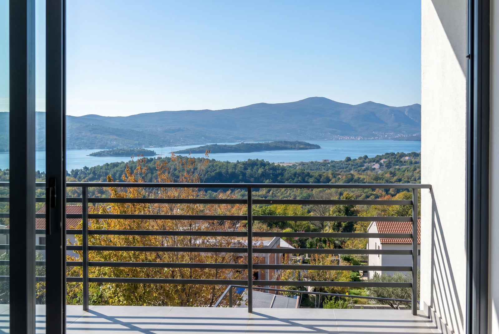 View from the townhouse balcony in Kavač, Montenegro: panoramic view of the Tivat Bay, mountains, and green hills on a clear day.