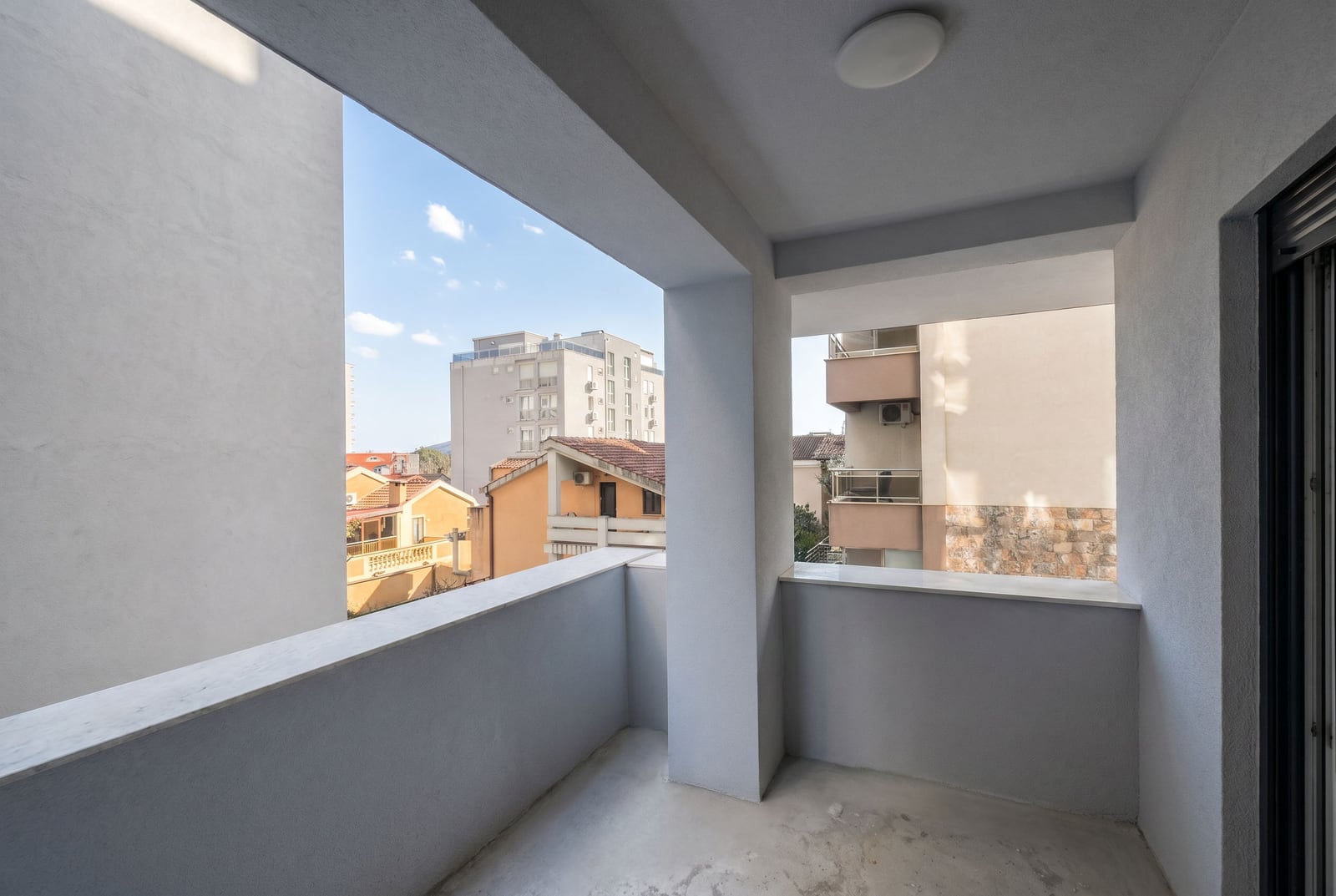 Spacious balcony with modern finishes in a Budva, Montenegro apartment, overlooking the cityscape.