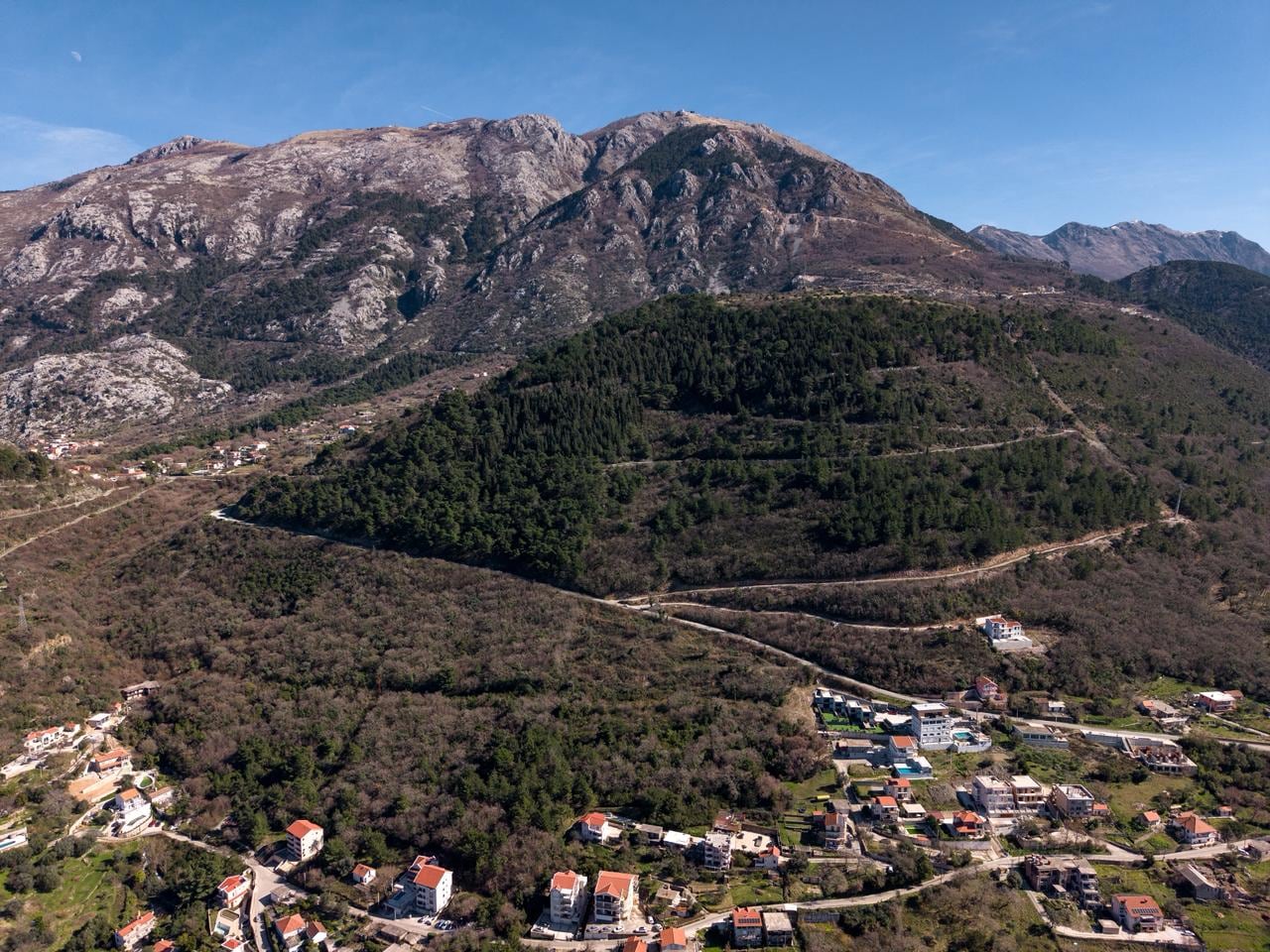 Panoramic view of a land plot in the mountains of Kotor, Montenegro: a picturesque landscape with forest and private houses.