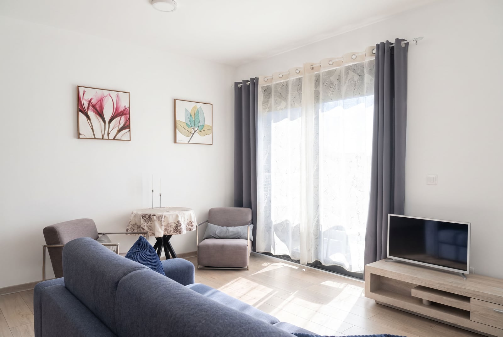 Modern living room with a blue sofa, TV, and panoramic window in an apartment in Budva, Montenegro