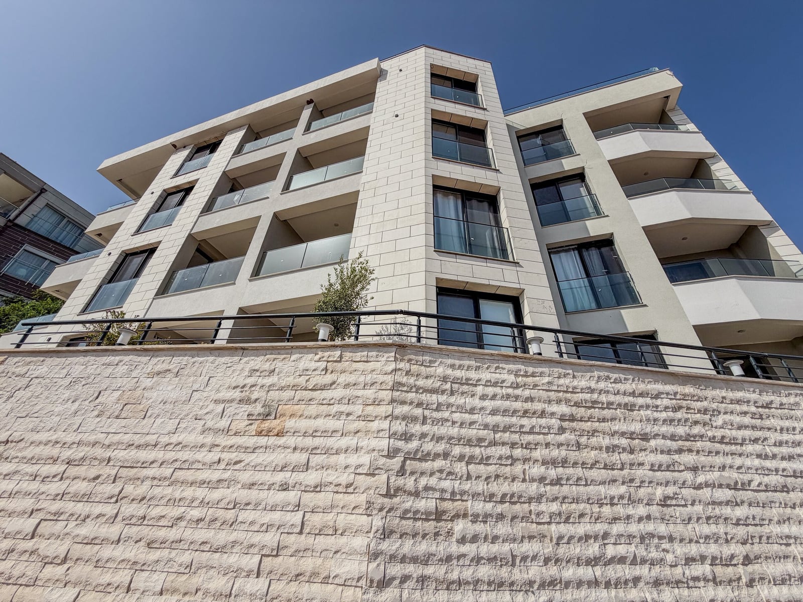 Low angle view of a modern multi-story apartment building with balconies and a stone retaining wall.