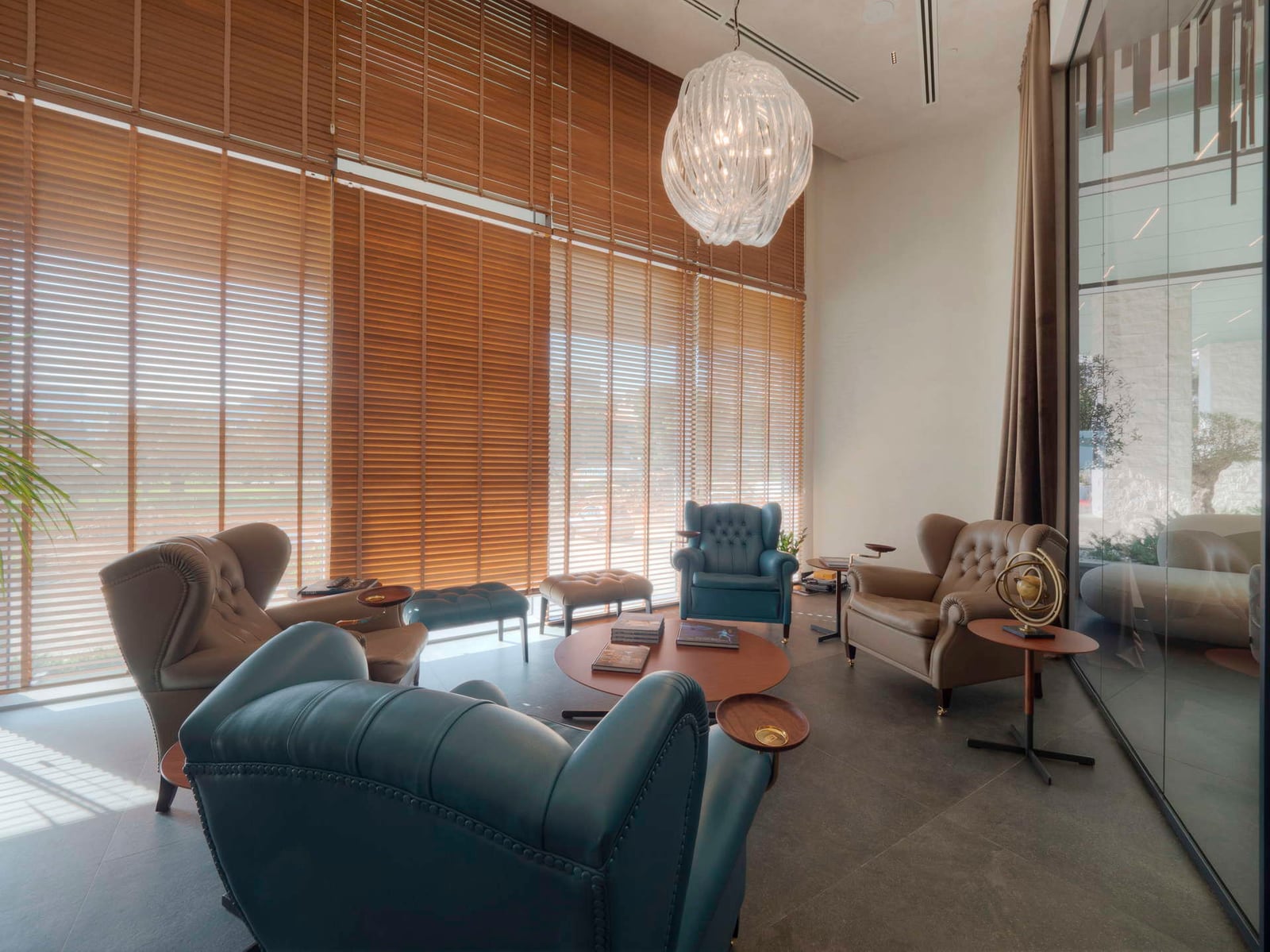 Modern living room featuring leather armchairs, wooden blinds, and a decorative glass pendant light.