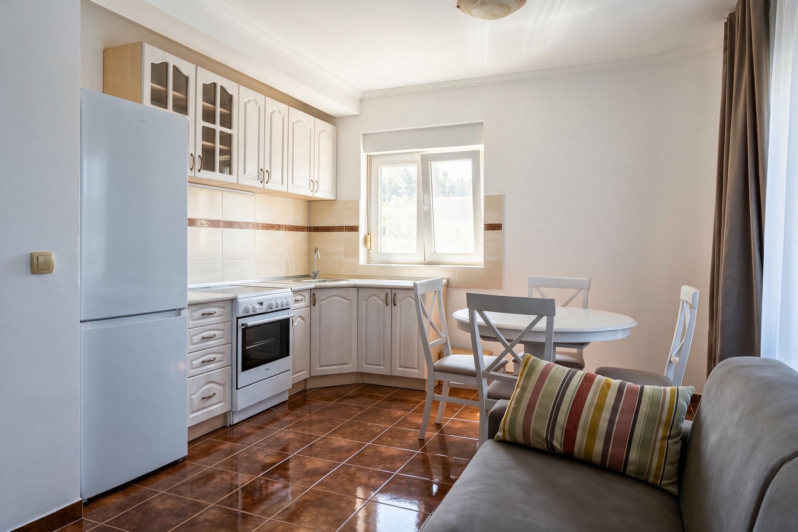 Bright kitchen-living room with white cabinetry, appliances, and a dining area in an apartment in Tivat, Montenegro.