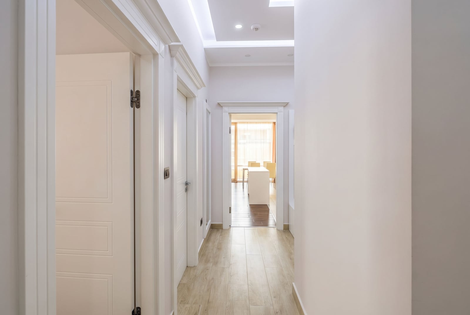 Bright hallway in a modern apartment in Budva, Montenegro: white doors, wood-look tile flooring, and a view into the living room.