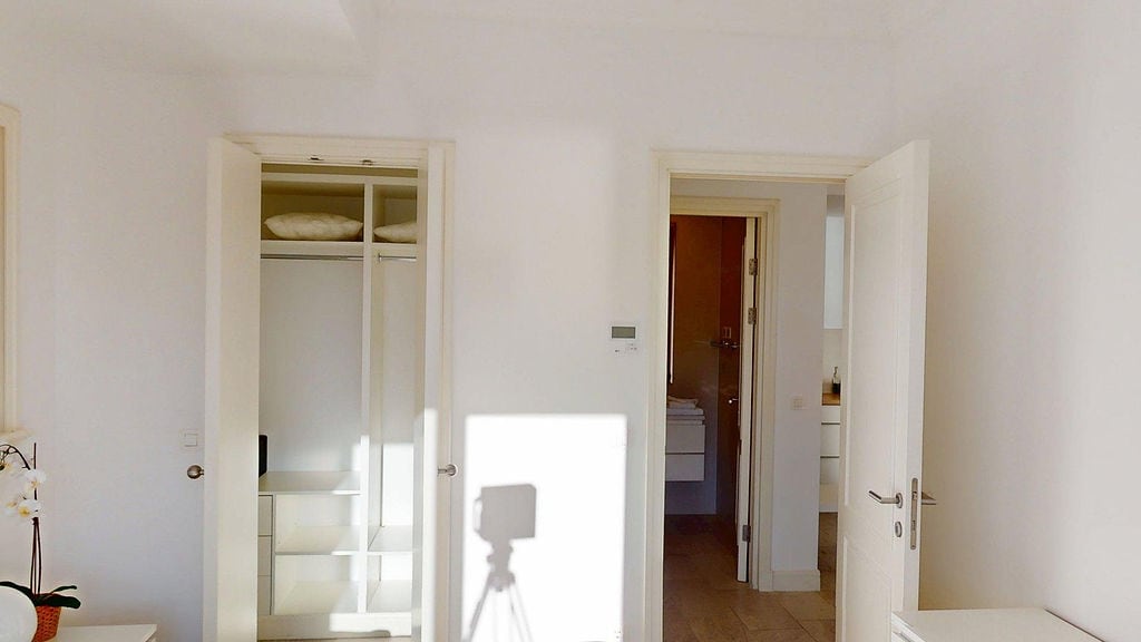 Bright bedroom in an apartment, Luštica, Montenegro: built-in wardrobe with shelves, white doors, and passage to the bathroom.
