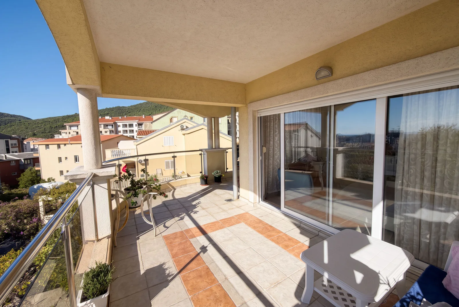 Tiled terrace with white plastic furniture and sliding glass doors overlooking a residential area and hills.