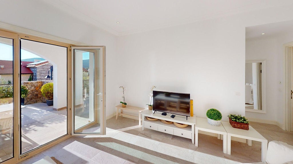 Bright living room with access to the terrace in a residential complex, Luštica, Montenegro: white furniture, TV area, and panoramic windows.