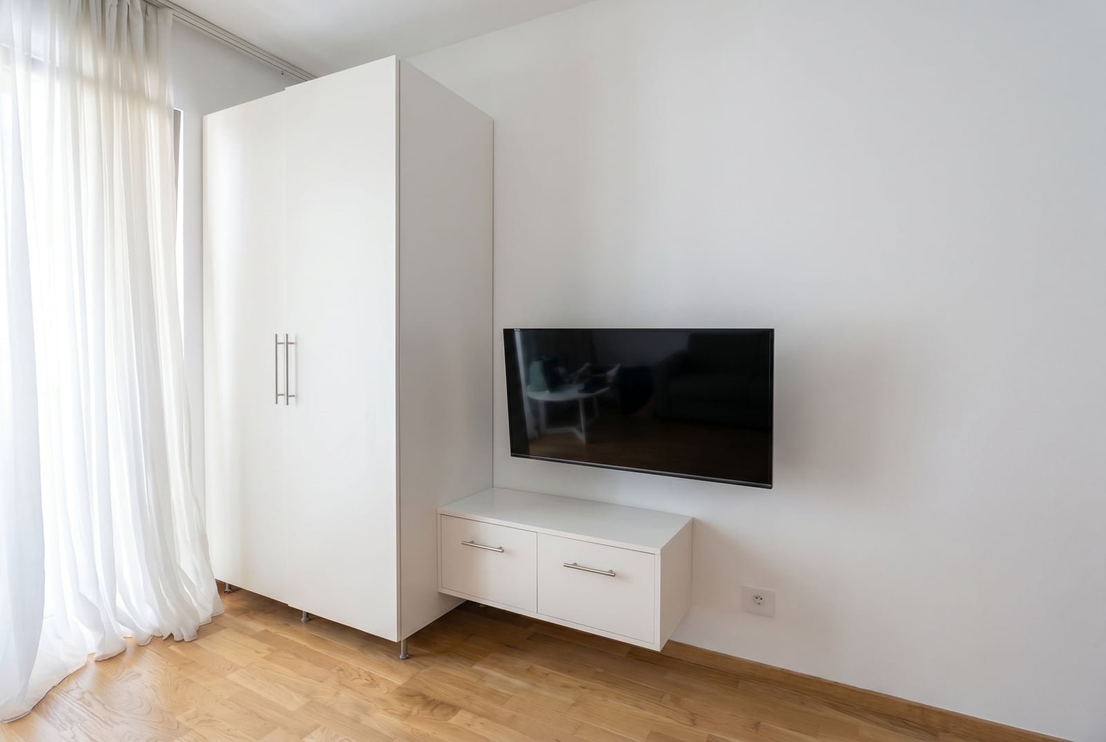 Modern living room with a white wardrobe, cabinet, and TV in an apartment in Bečići, Montenegro. Bright interior with parquet flooring.