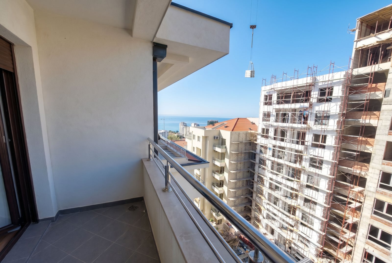 Apartment balcony in Rafailovici, Montenegro, with a sea view and residential buildings under construction with metal scaffolding.
