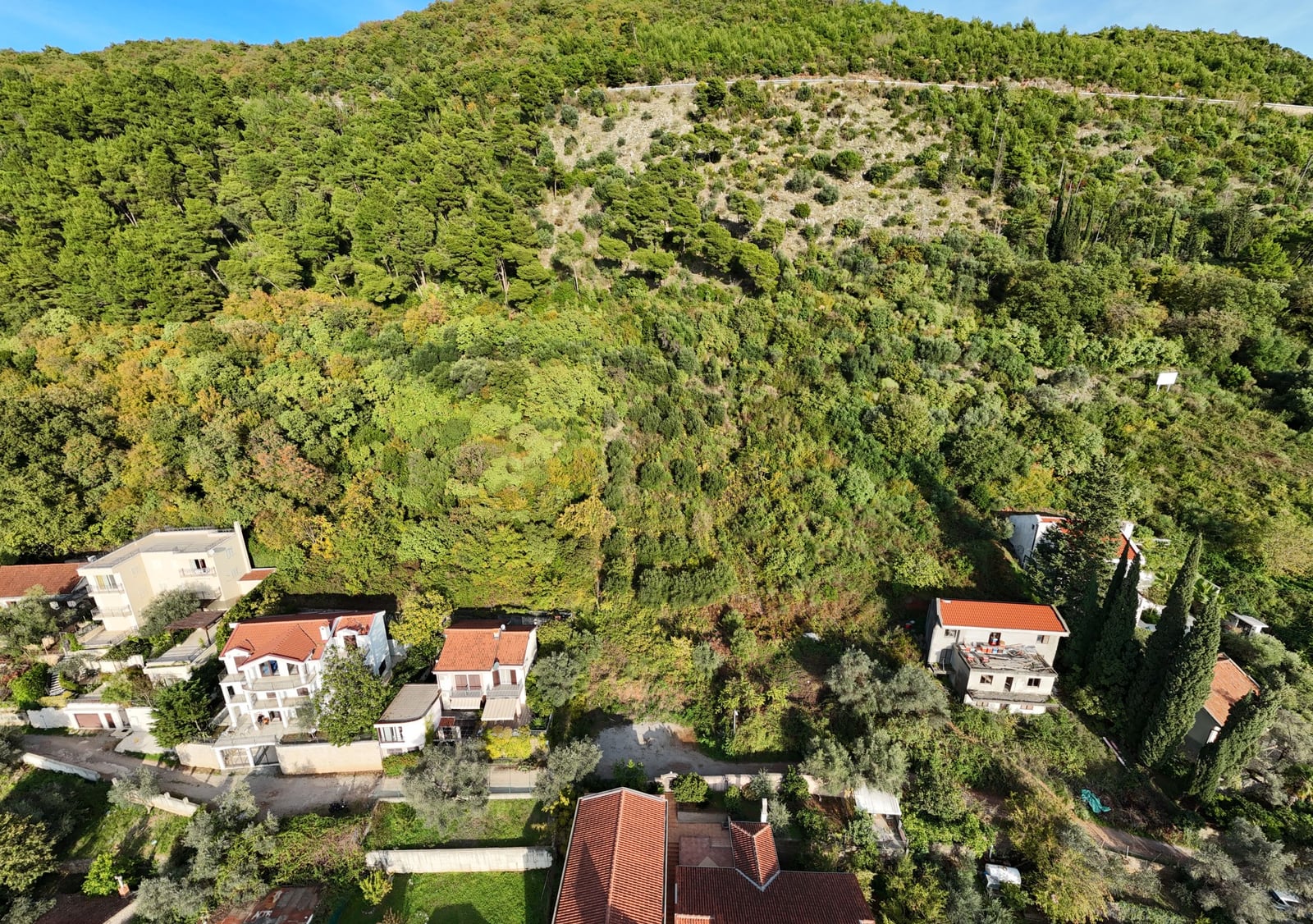 Building plot in Budva, Montenegro: aerial view of houses at the foot of a green, forested hill.