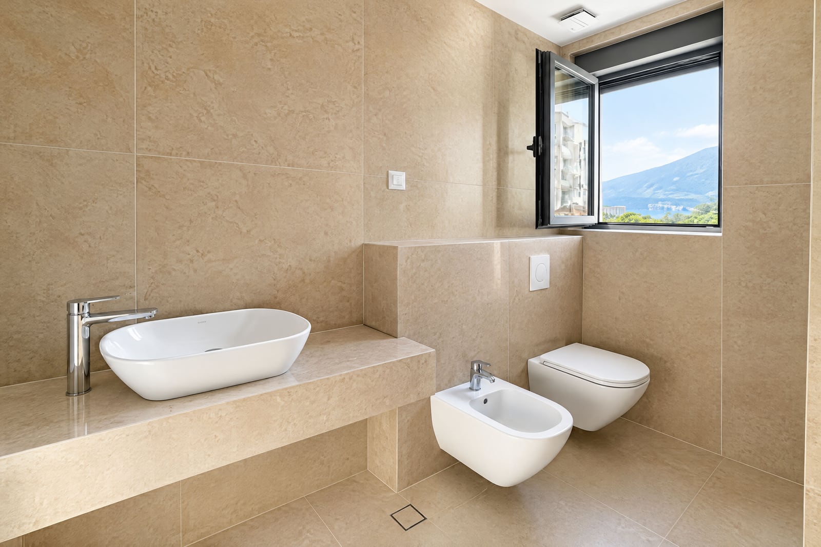 Modern bathroom with beige tiles, a vessel sink on a stone counter, wall-mounted toilet, and bidet.