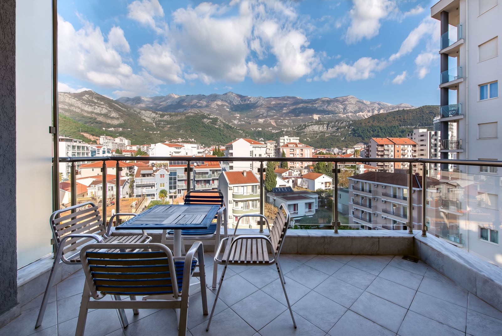 Balcony with outdoor table and chairs overlooking a city and mountains.
