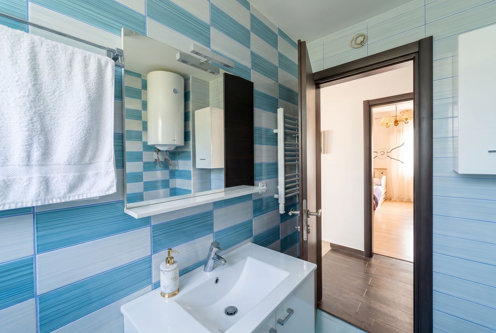 Bathroom with blue tiles and a water heater in an apartment for sale, Kumbor, Montenegro. View of the bedroom.