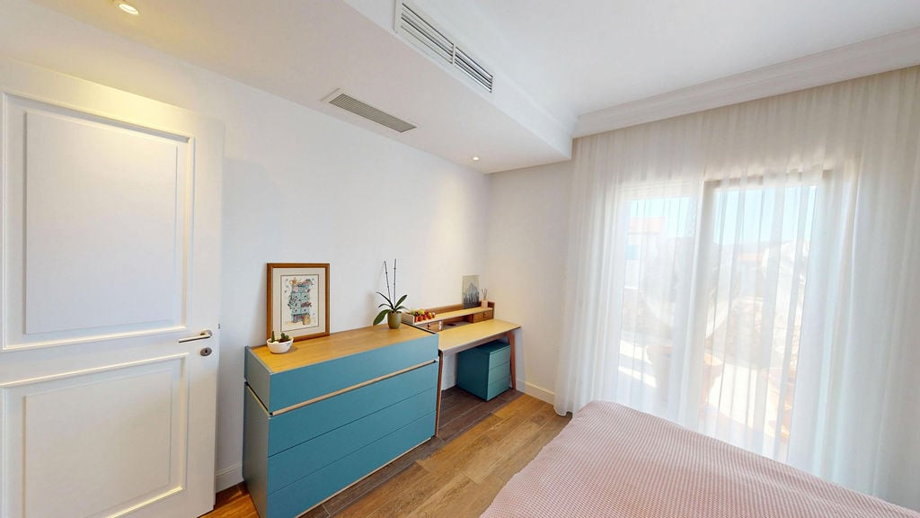 Bright bedroom with a blue dresser and desk in the apartment of the Luštica residential complex, Montenegro. Modern interior with a panoramic window.