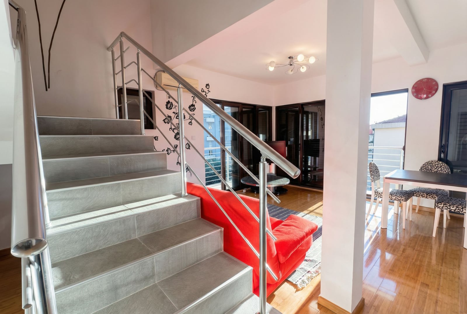 Living room in an apartment in Bečići, Montenegro: staircase with metal railings, red sofa, and dining area.
