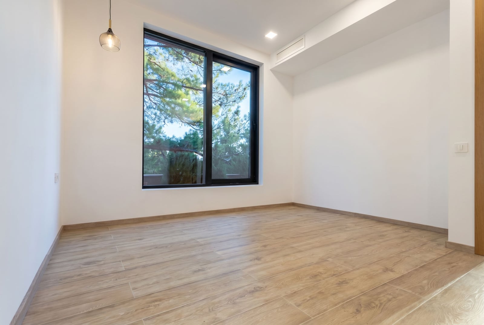 Bright living room with a panoramic window and a view of pine trees in a villa, Kavač, Montenegro: modern finishes and wood-look tile.