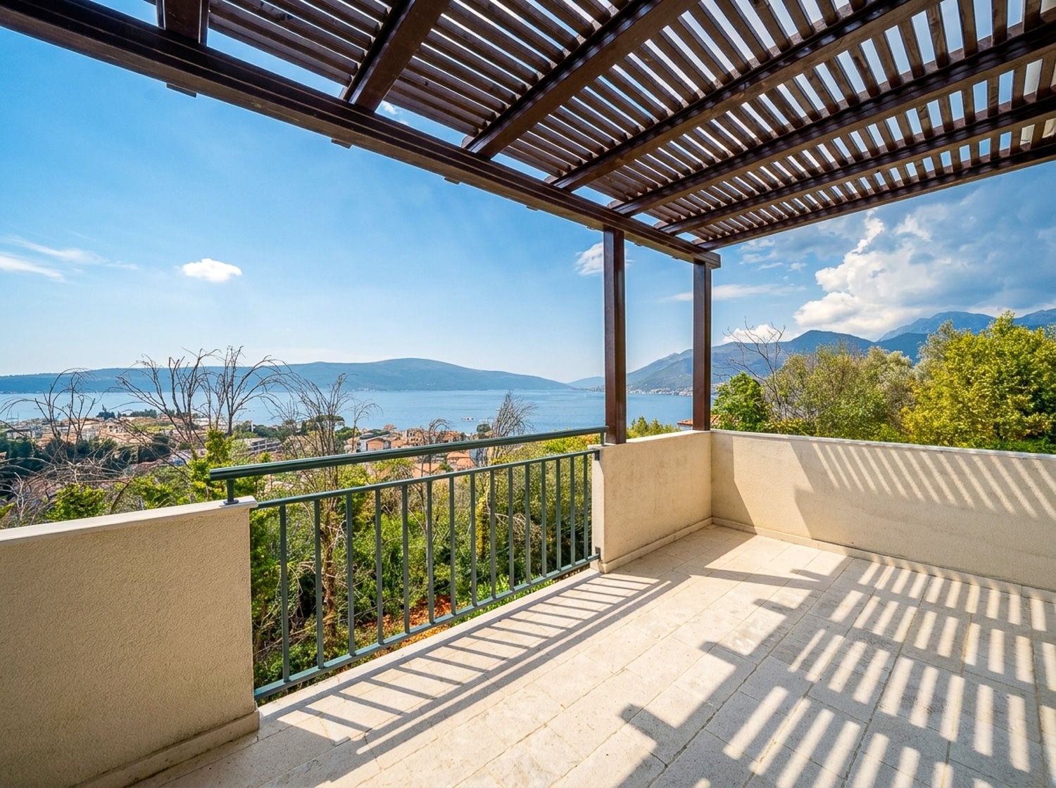 Balcony with wooden pergola and metal railing overlooking the sea and mountains.