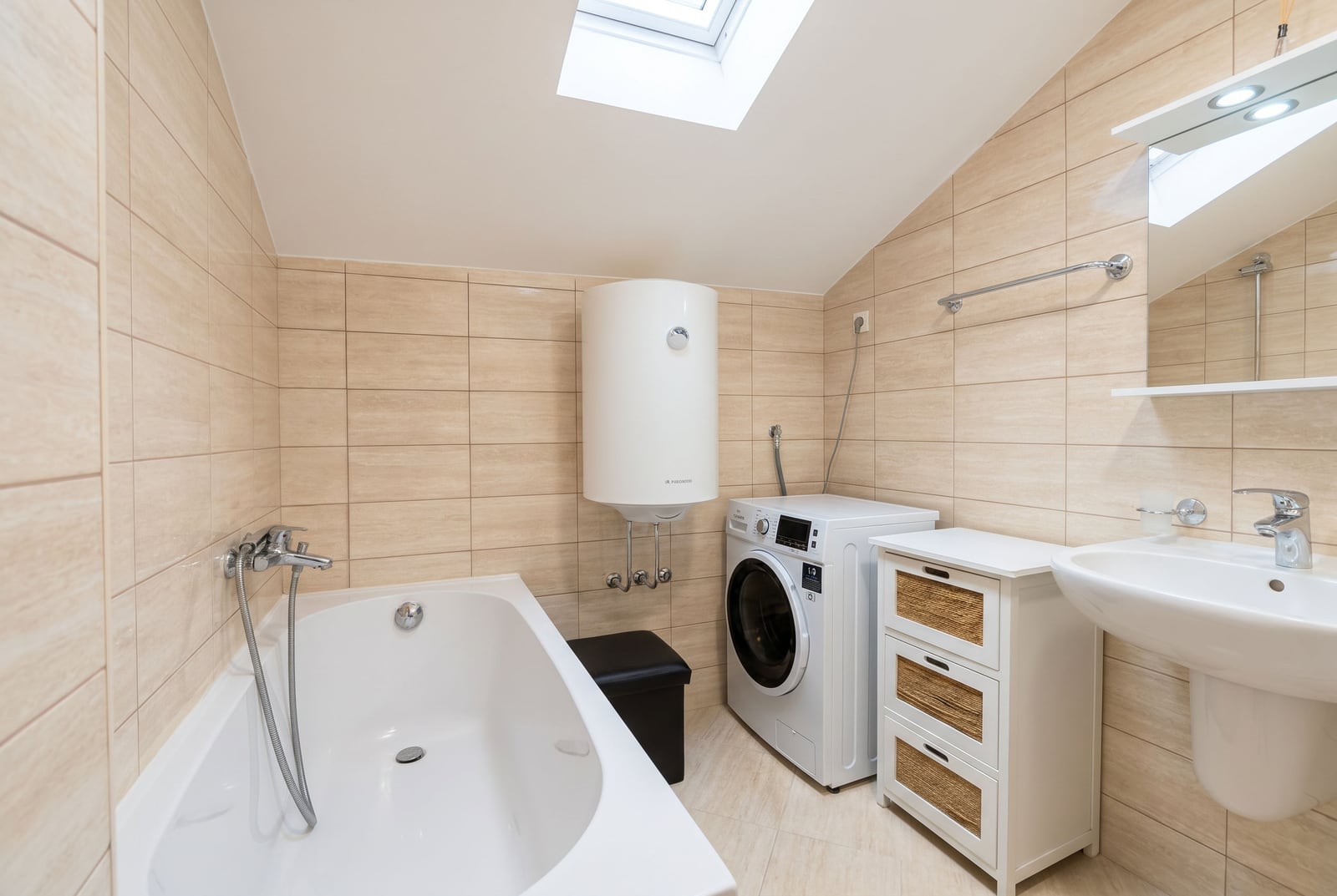 Bathroom in a Budva apartment, Montenegro: beige tiles, bathtub, washing machine, and skylight.