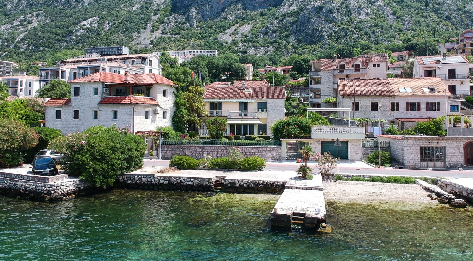 Villa in Dobrota, Montenegro: view of the house with stone cladding, a private pier, and the shoreline of the Bay of Kotor.