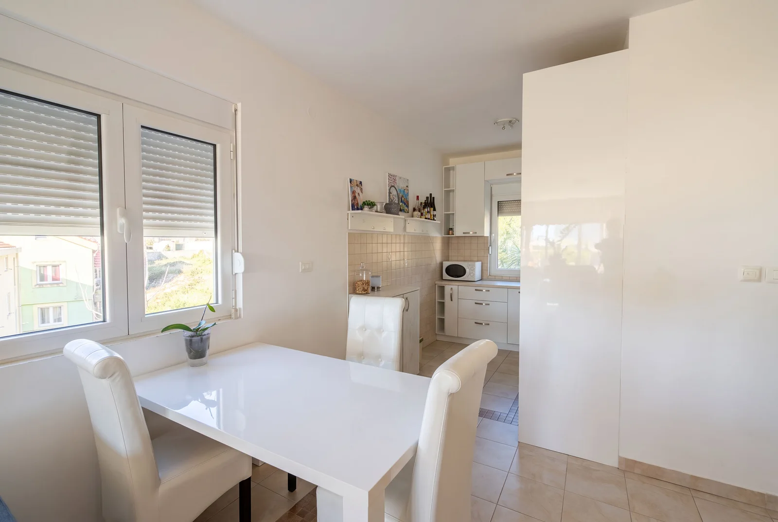 Dining area with white table and chairs adjacent to a kitchen with cabinets and microwave.
