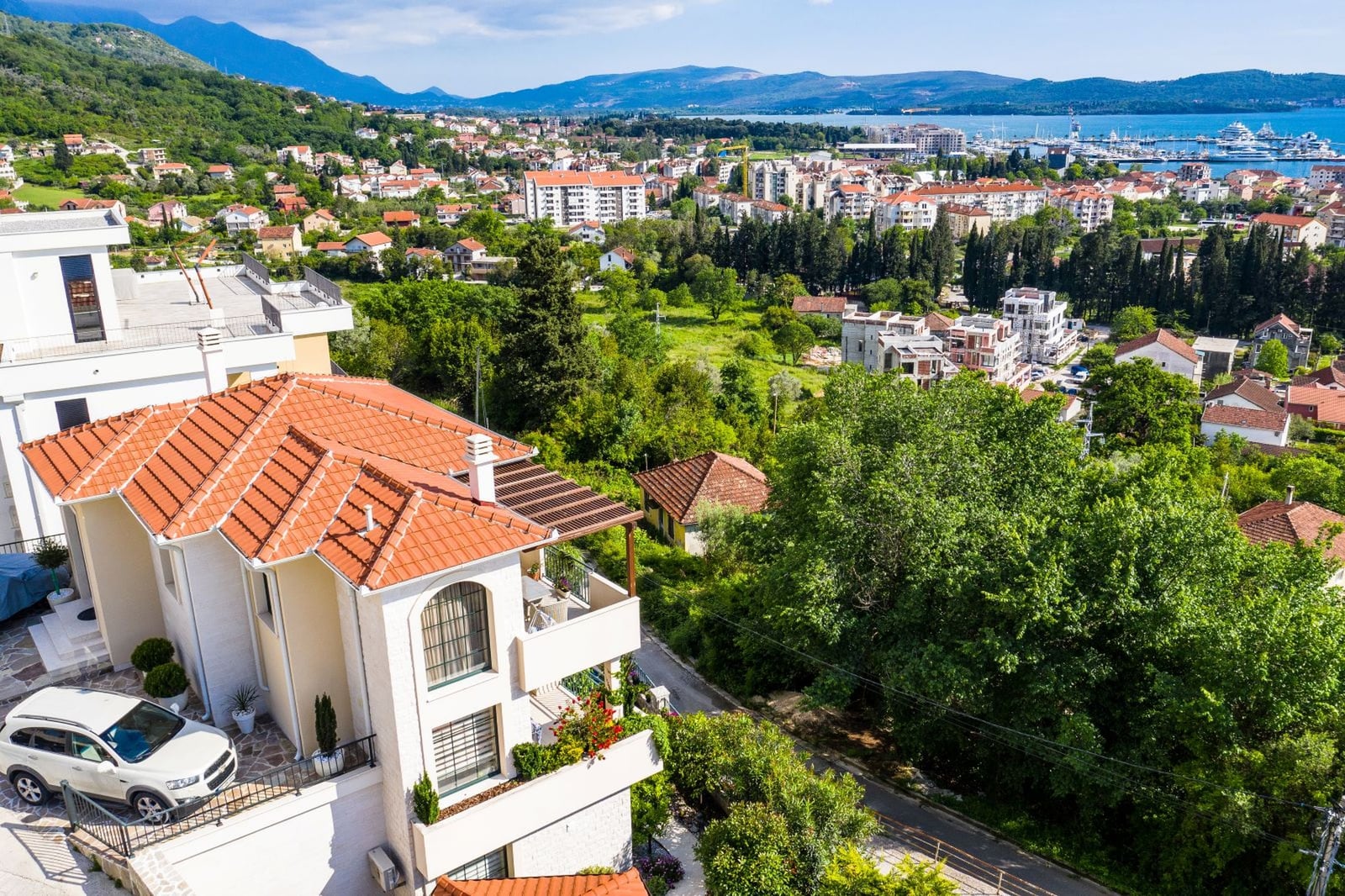 Aerial view of a villa in Tivat, Montenegro: a house with a tiled roof, terrace, and panoramic views of the bay and mountains.