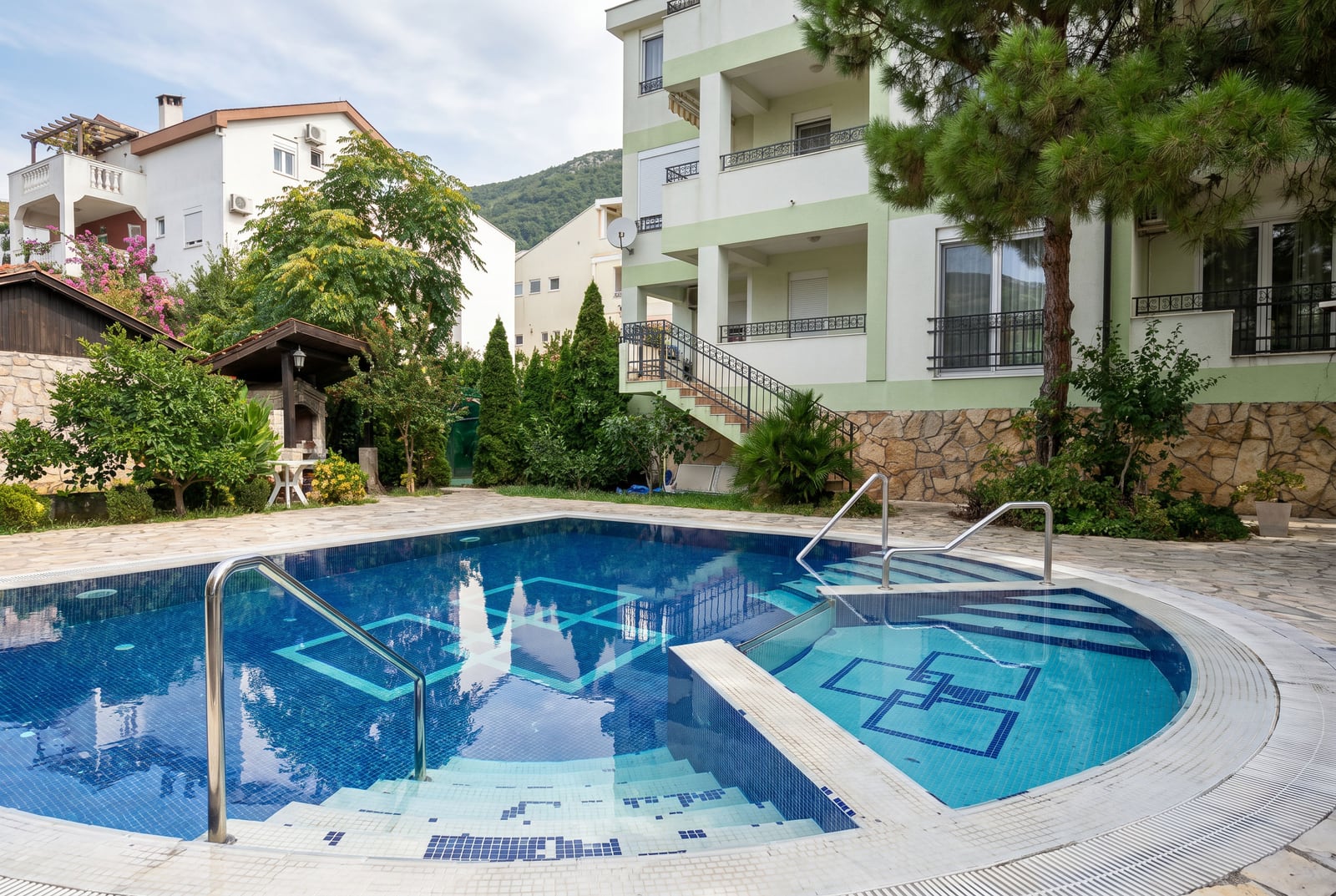 Outdoor swimming pool at a residential building in Budva, Montenegro, featuring a lounge area, barbecue facilities, and landscaped grounds.