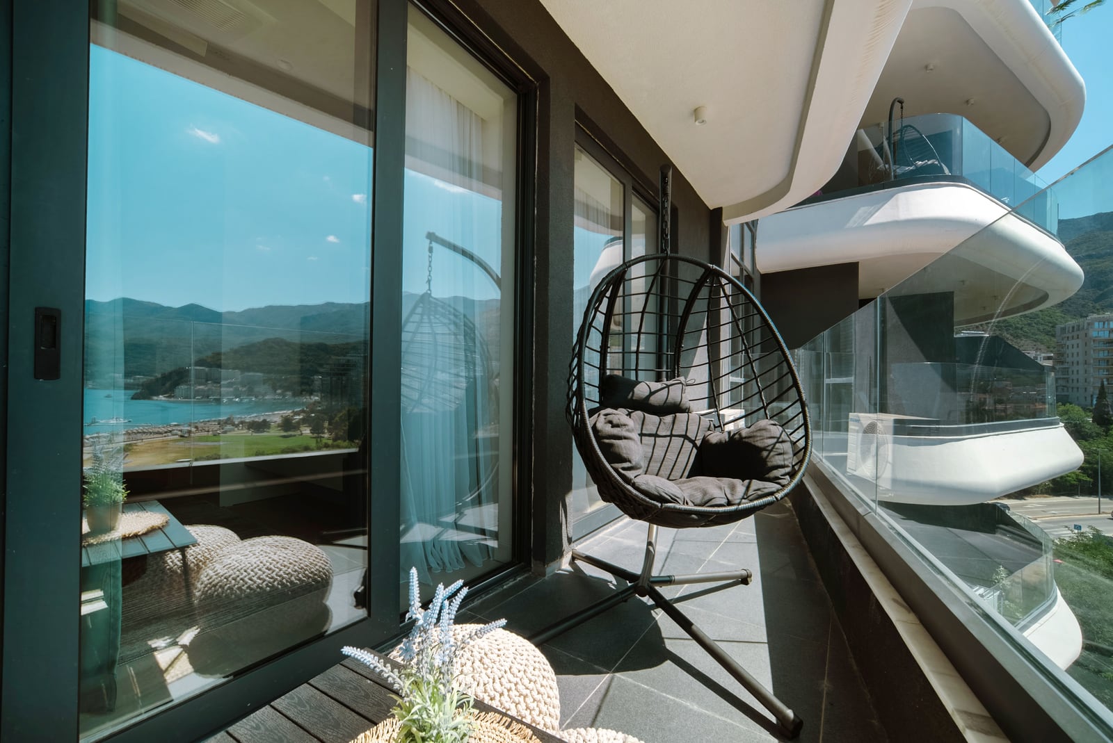 Balcony of a modern apartment in Bečići, Montenegro, with a hanging chair and panoramic views of the sea and mountains.
