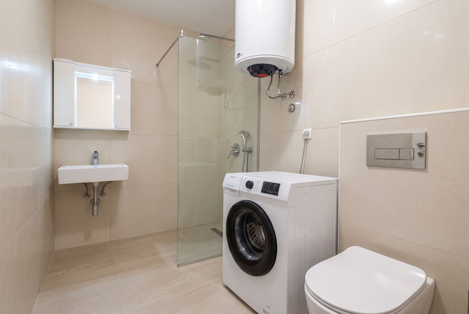 Bathroom featuring a shower, sink, toilet, and washing machine with beige tiled walls.