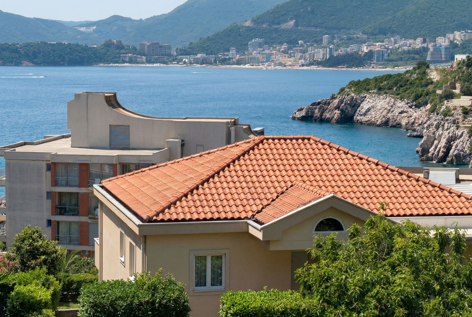 Sea and coastline view of the Budva Riviera from an apartment in Pržno, Montenegro: houses with tiled roofs and greenery.