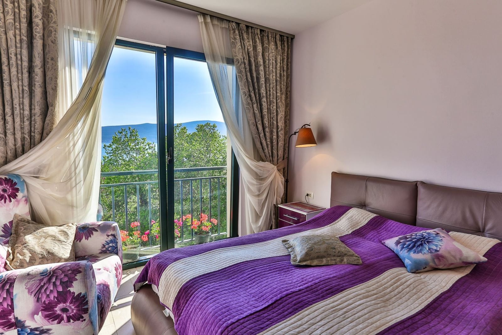 Bedroom with sea and mountain views in a villa in Tivat, Montenegro: double bed, armchair, and balcony access.