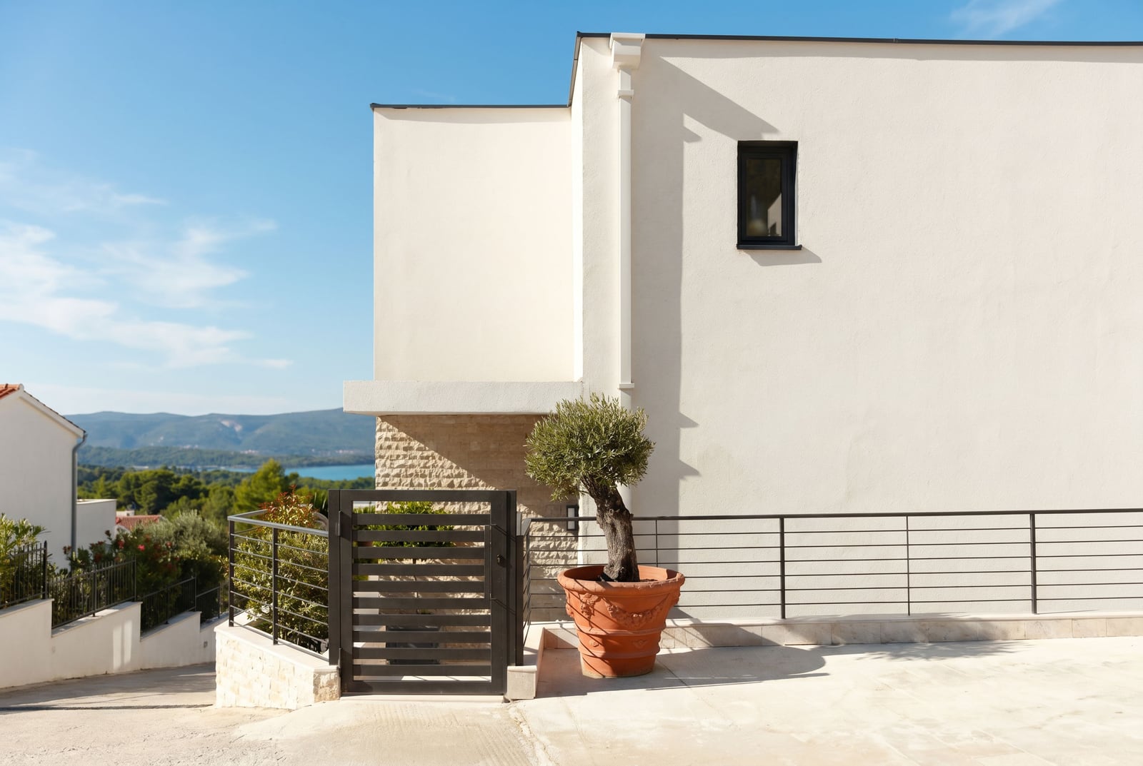 Modern townhouse in Kavač, Montenegro: bright facade, stone detailing, olive tree, and sea view.