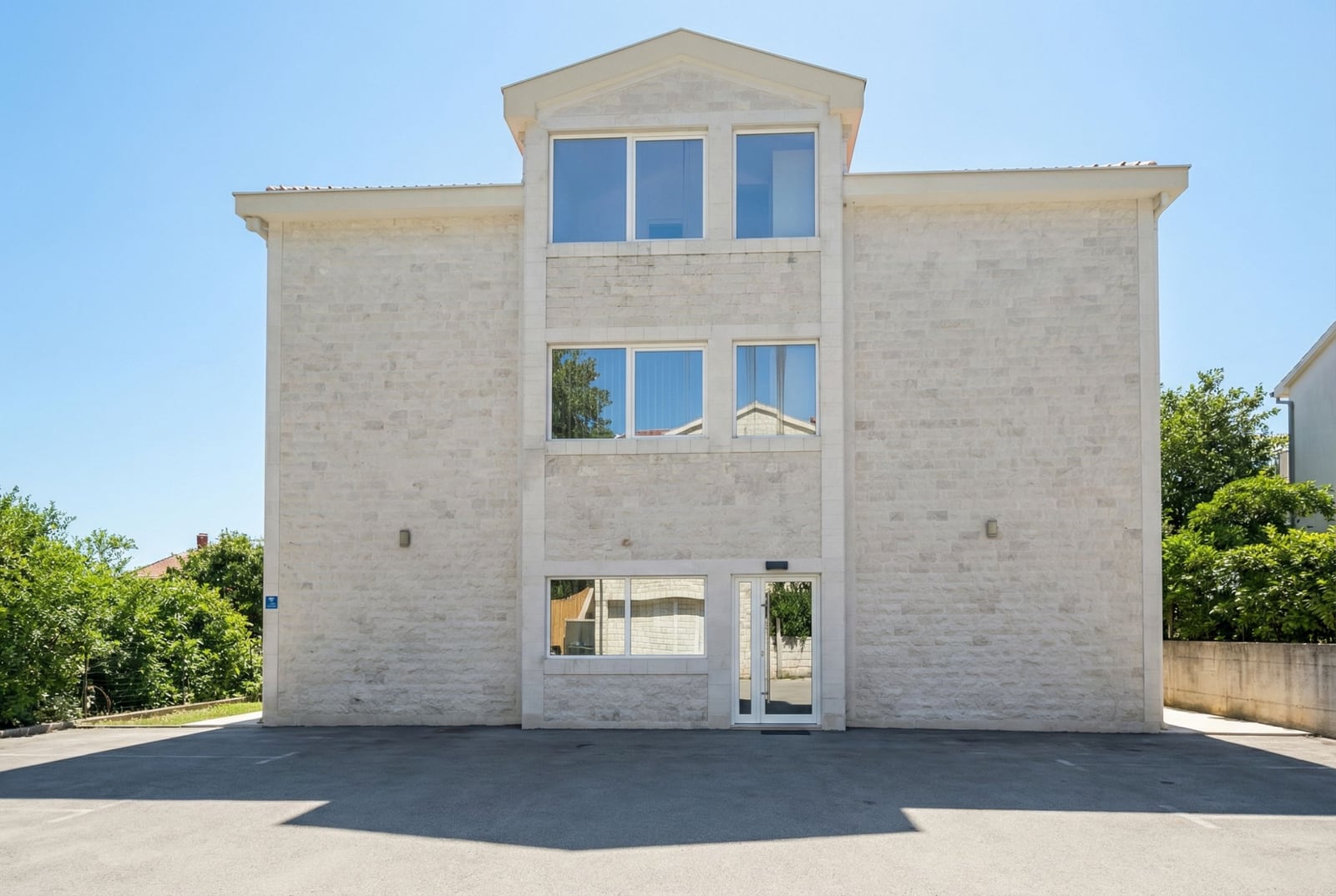 Three-story residential building with a light stone facade and parking in Tivat, Montenegro.