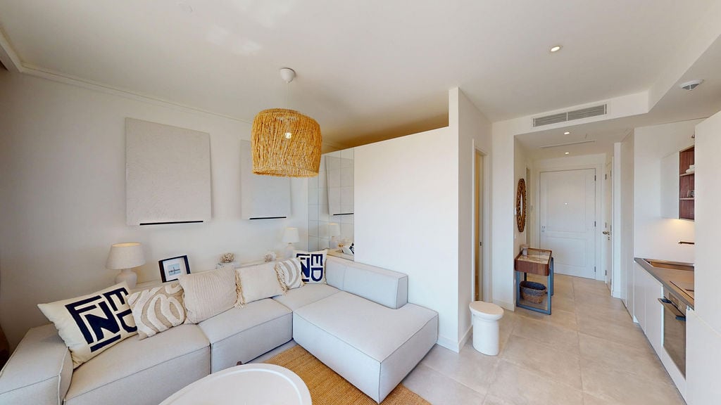 Modern living room with kitchen in light tones in the Luštica residential complex, Montenegro: corner sofa, woven lamp, and decor.