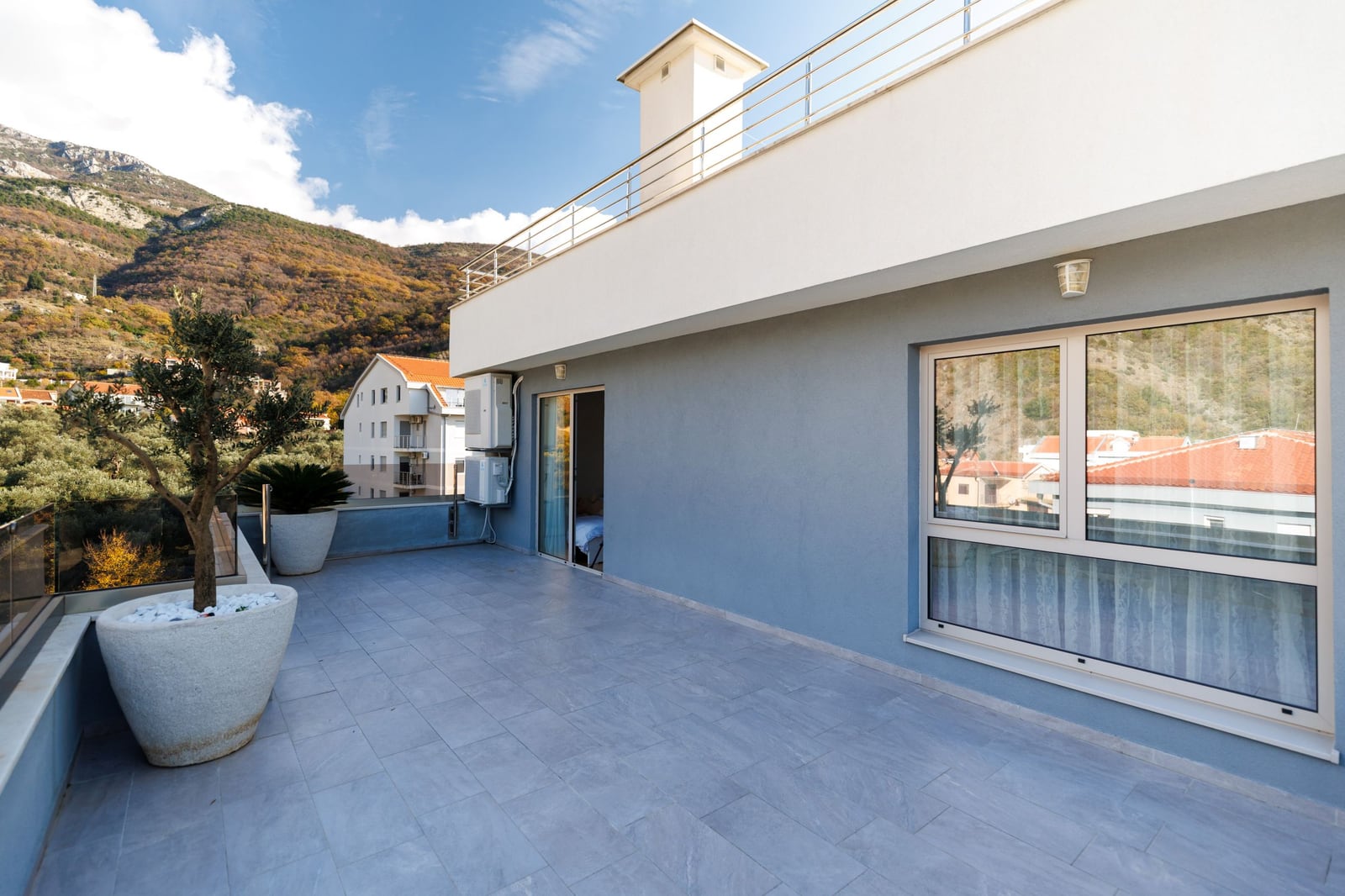 Spacious penthouse terrace in Bečići, Montenegro, featuring mountain views, modern finishes, and decorative trees.