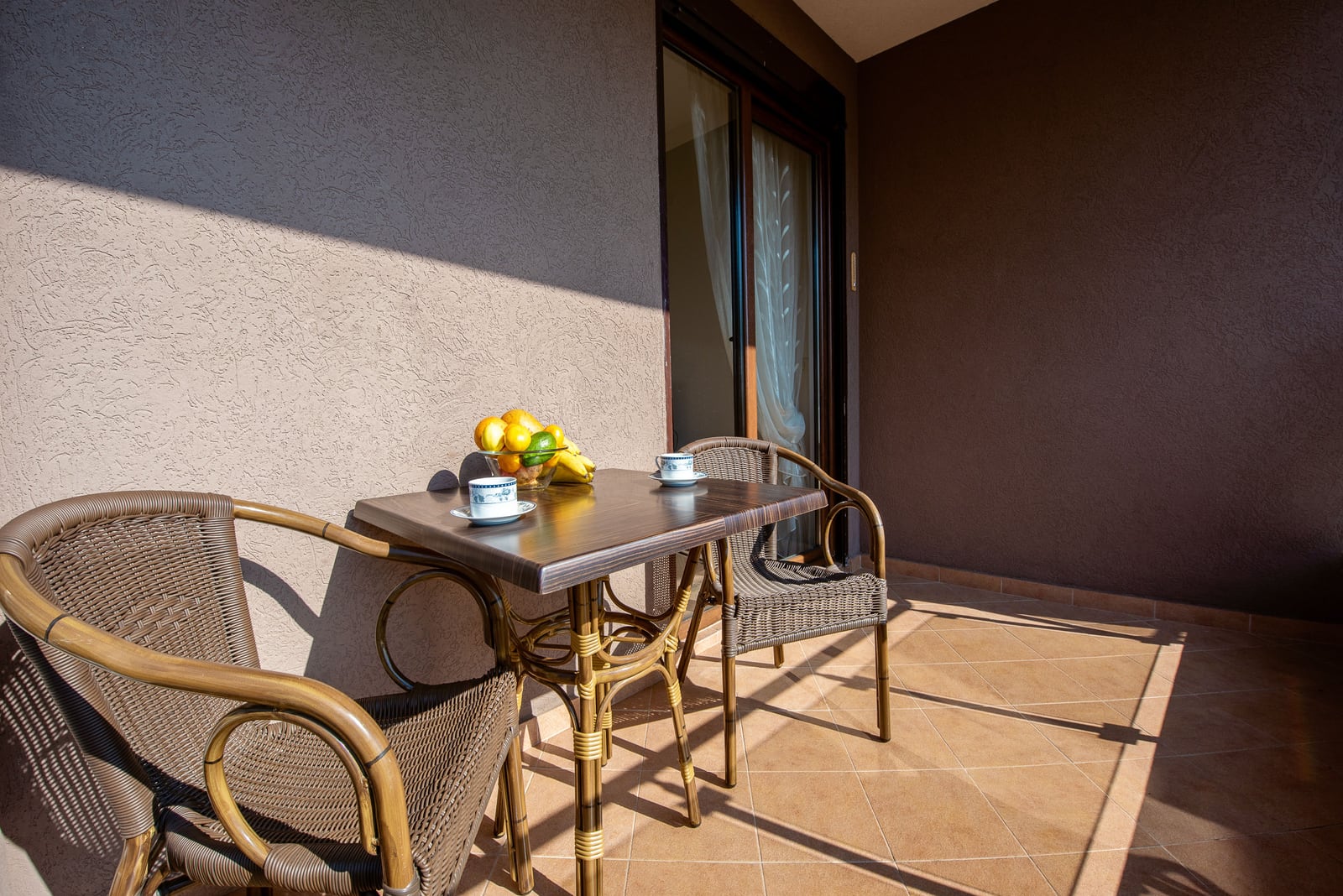 Cozy balcony with wicker furniture and a table in an apartment, Budva, Montenegro: view of the terrace with tiles and fruit.