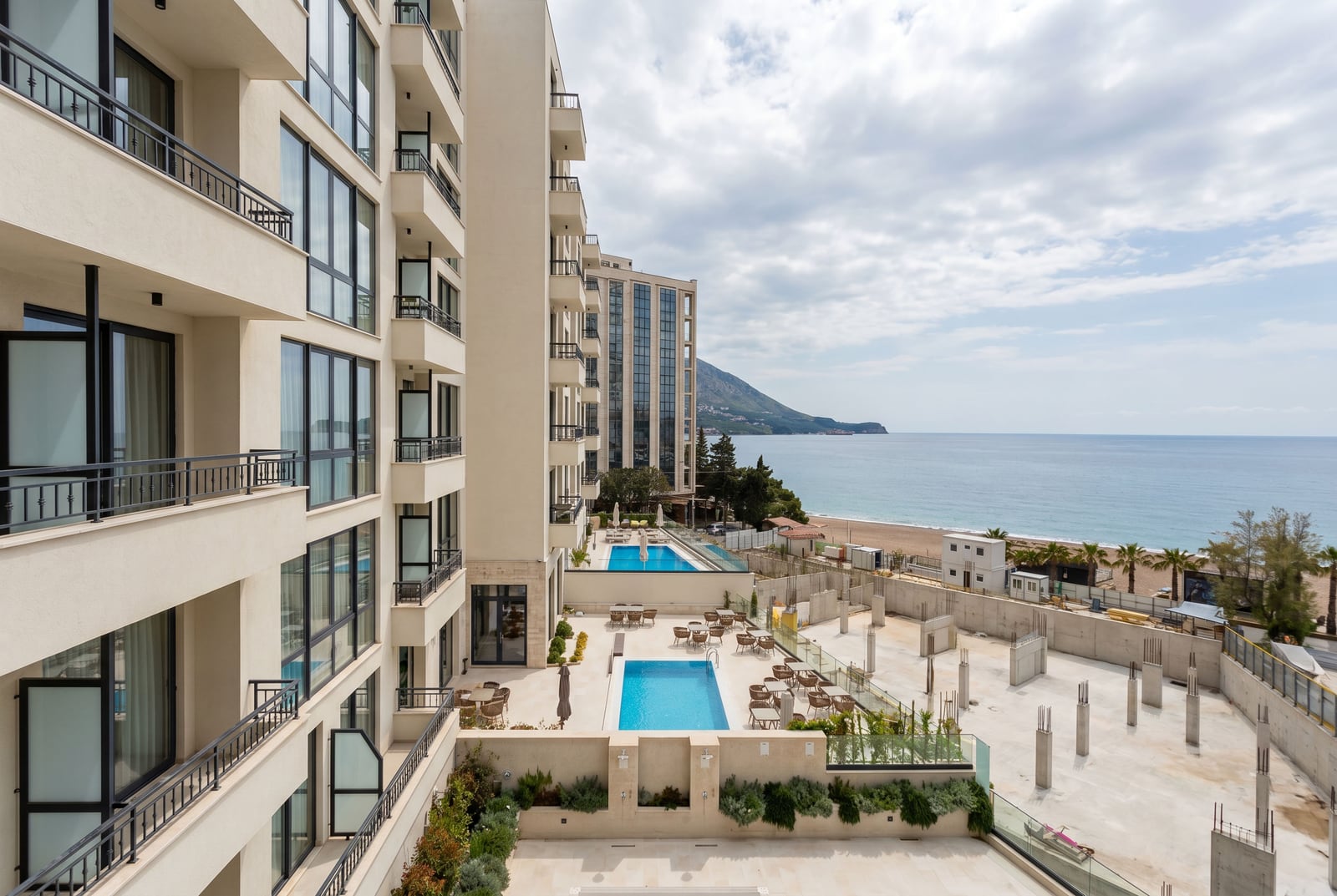 Modern residential complex in Becici, Montenegro: view of the swimming pools, terrace, and the coastline with the beach.