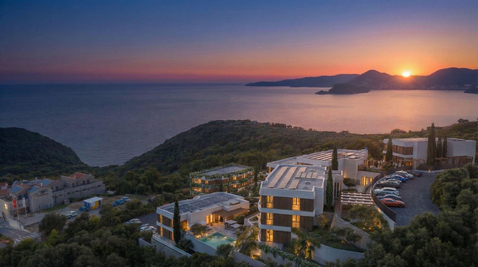 Panoramic exterior view of a modern coastal hotel complex at sunset with mountains and sea.