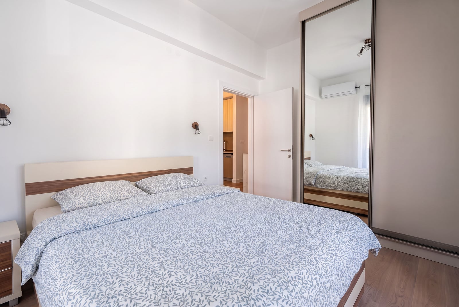 Bedroom featuring a double bed with blue leaf-pattern bedding and a large wardrobe with a mirror door.