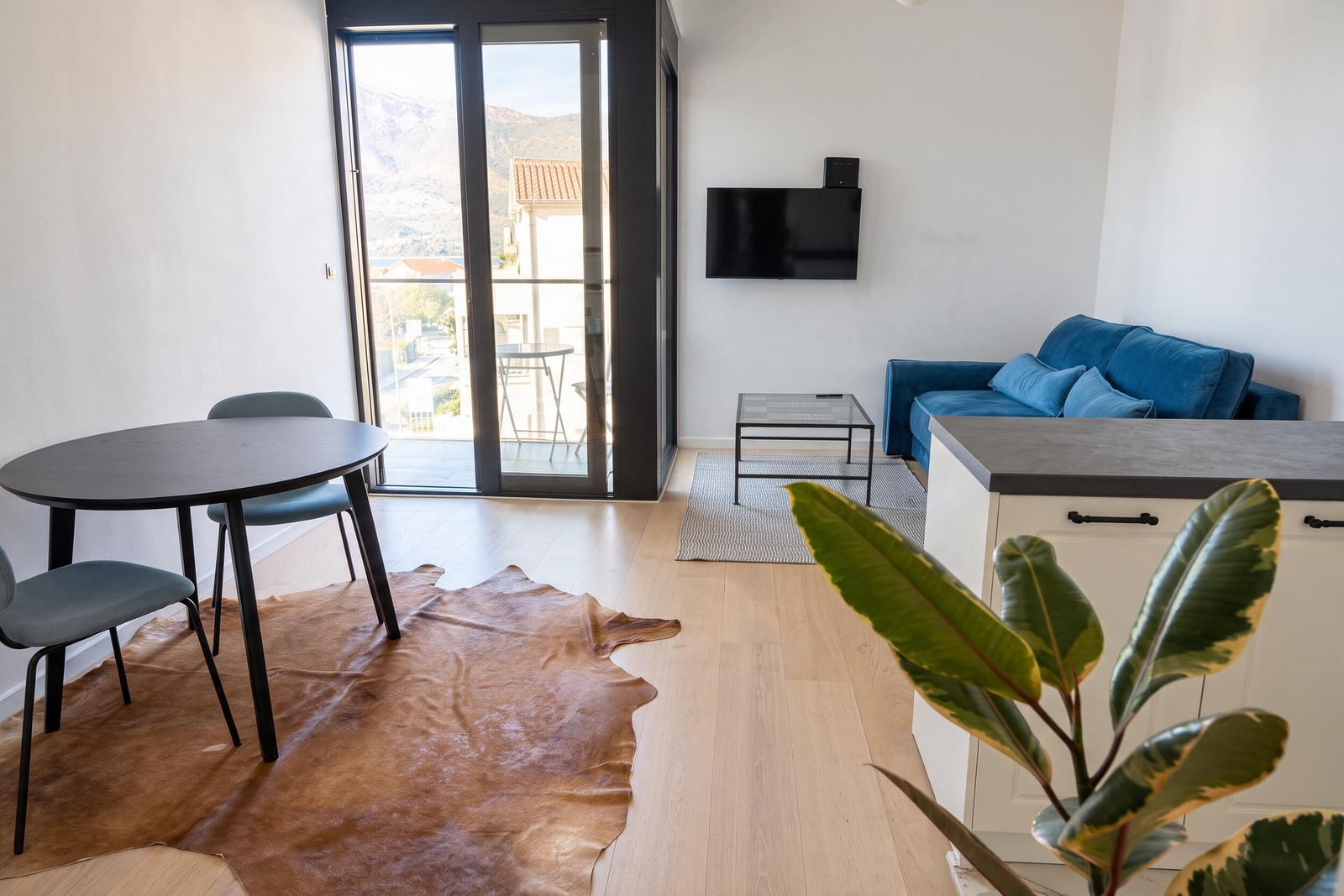 Modern living room with a blue sofa, dining area, and panoramic window in Tivat, Montenegro