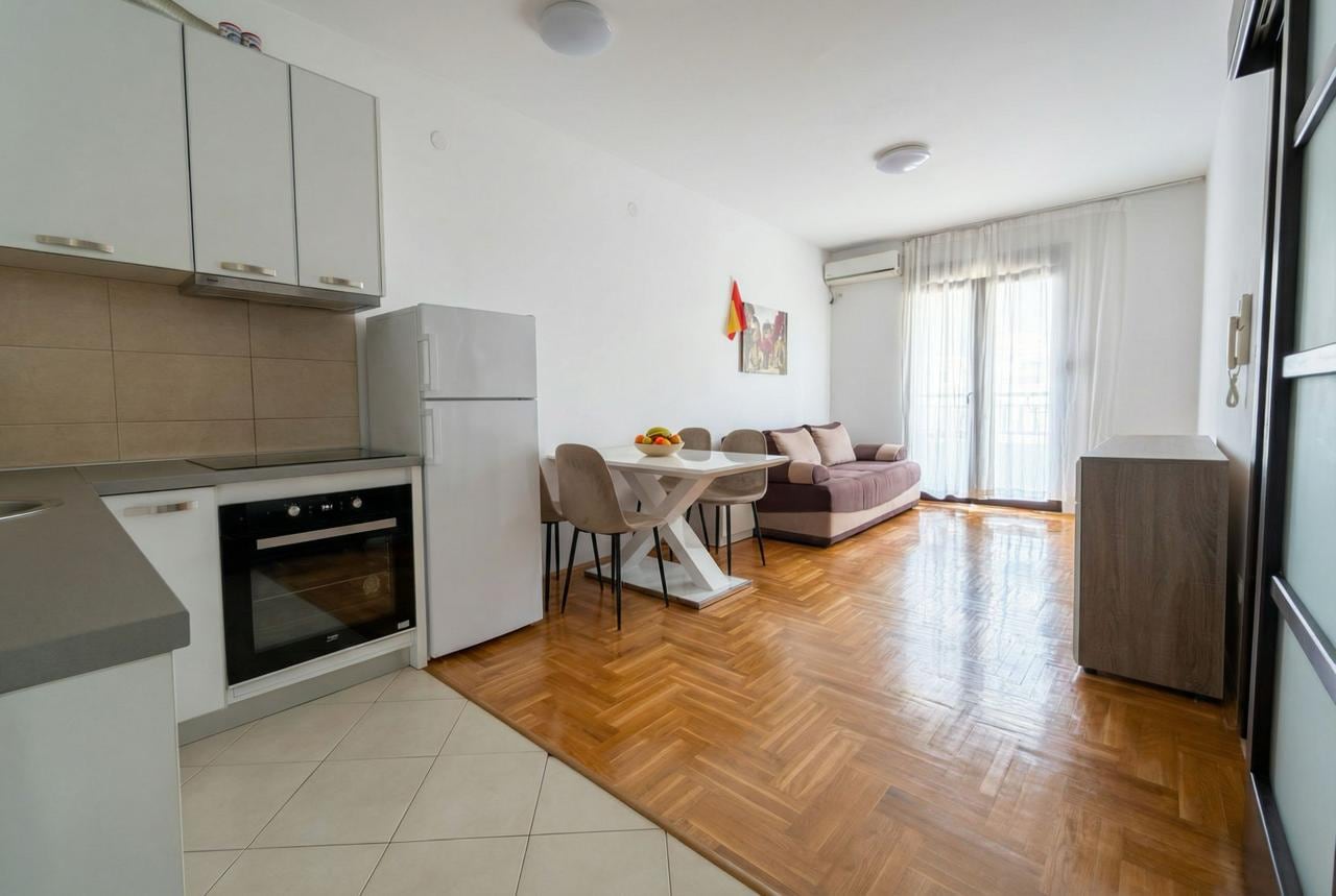 Modern kitchen-living room with dining area in an apartment in Budva, Montenegro: light furniture, parquet flooring, and access to the balcony.