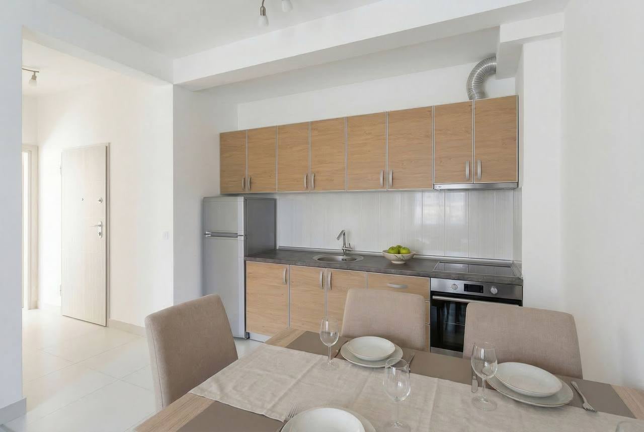 Modern kitchen with light-colored furniture and a dining area in an apartment in Bečići, Montenegro.
