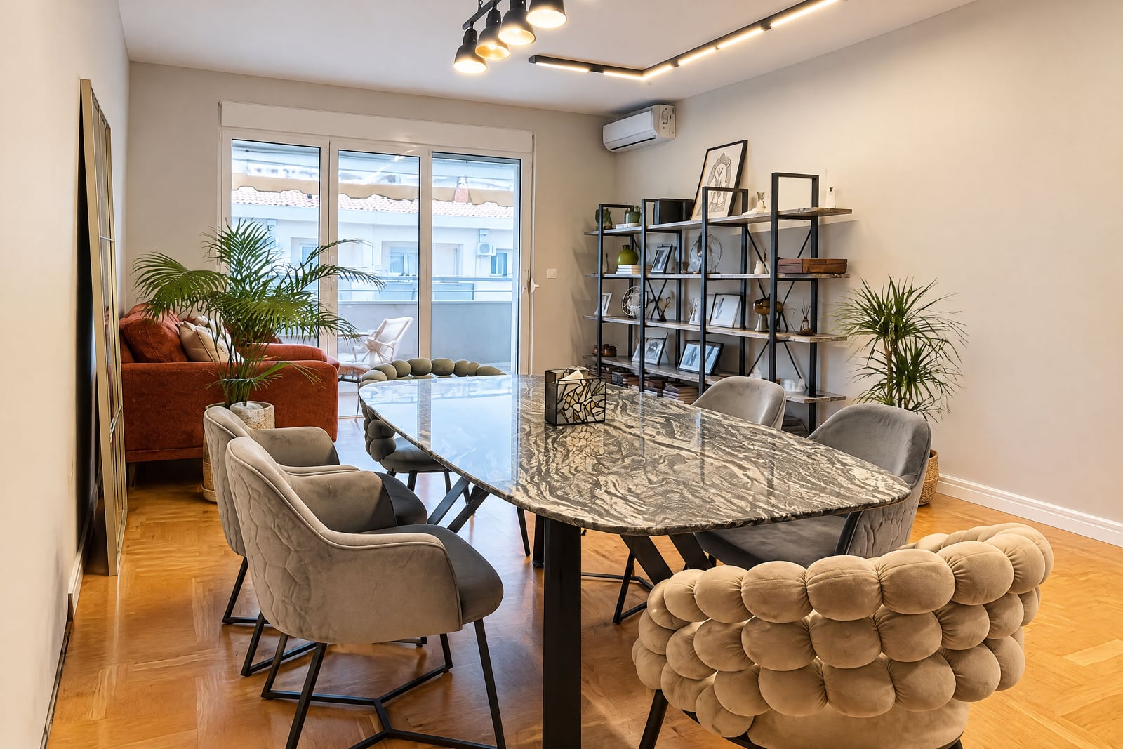 Living room featuring a marble dining table, grey velvet chairs, an orange sofa, and open shelving.