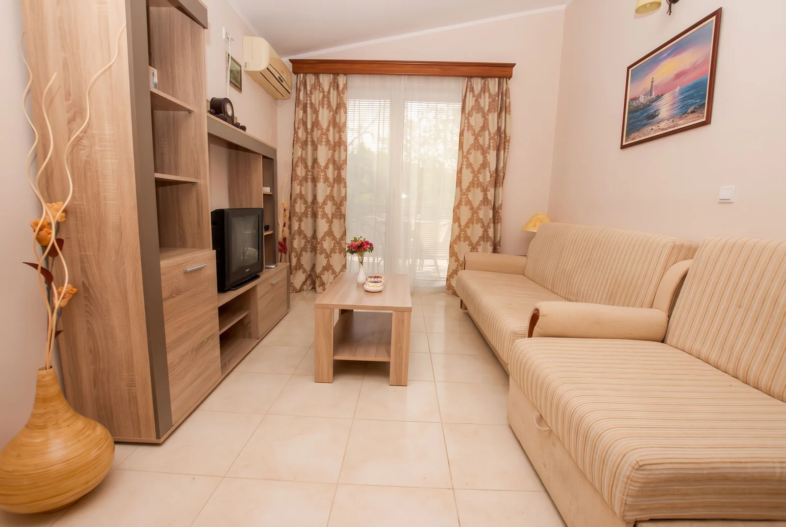 Living room featuring a beige striped sofa, wooden TV unit, coffee table, and patterned curtains.