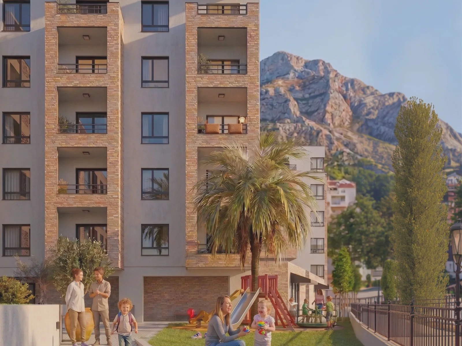 Exterior of a multi-story apartment building with balconies, a palm tree, and a playground against mountains.