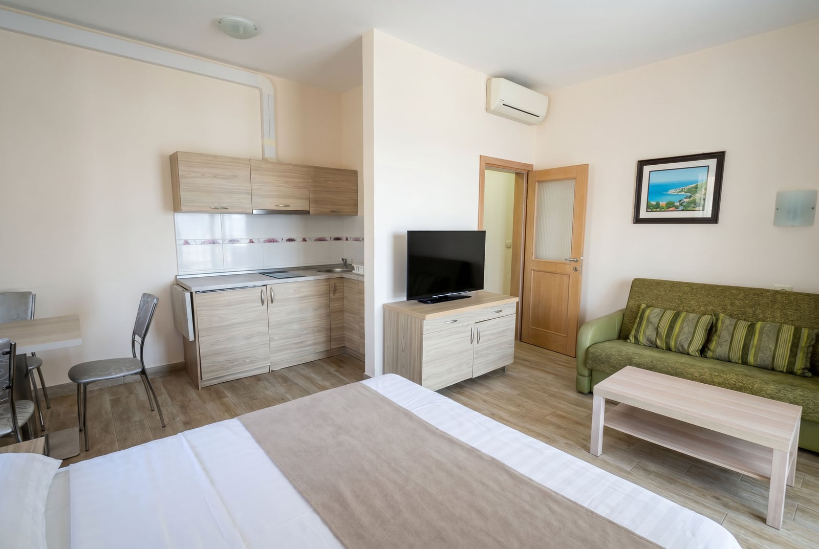 Interior of a studio apartment in Becici, Montenegro: kitchen, lounge area with a sofa, TV, and a double bed.