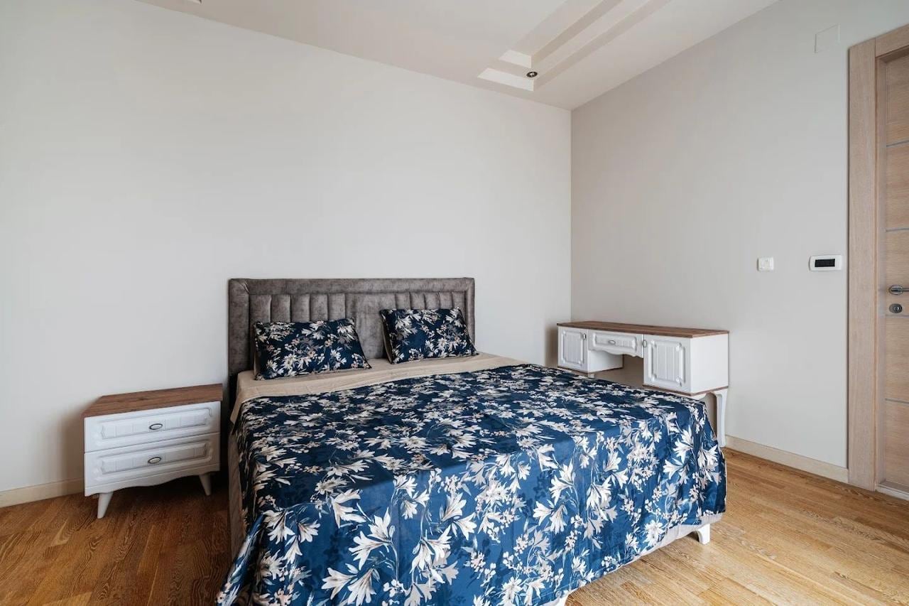 Bedroom in an apartment in Budva, Montenegro: a double bed with a soft headboard, white furniture, and parquet flooring.