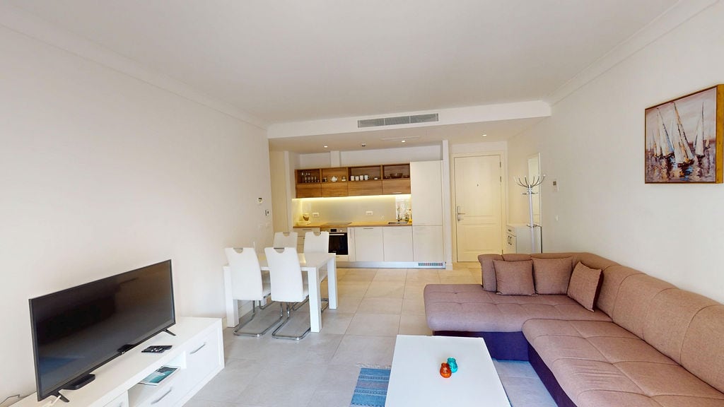 Modern living room with kitchen in an apartment, Luštica, Montenegro: corner sofa, dining area, and light-colored finishes.