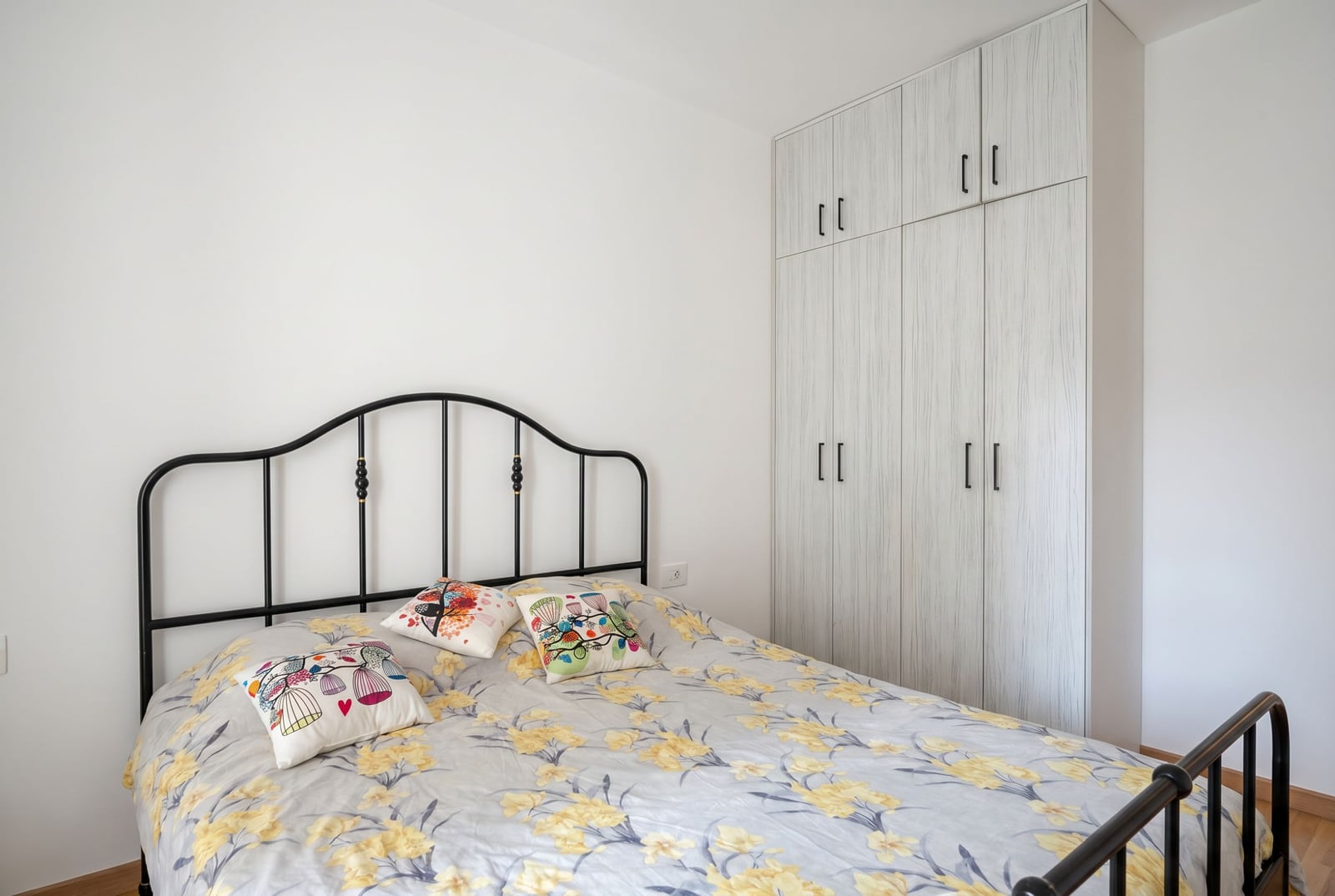 Bedroom in an apartment in Becici, Montenegro: a double bed with a wrought-iron headboard and a built-in light-colored wardrobe.