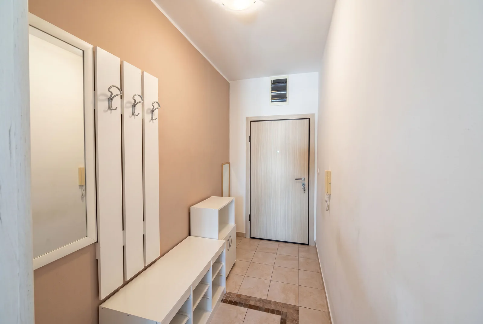 Entryway featuring white storage units, coat hooks, a bench, and a main entrance door at the end.