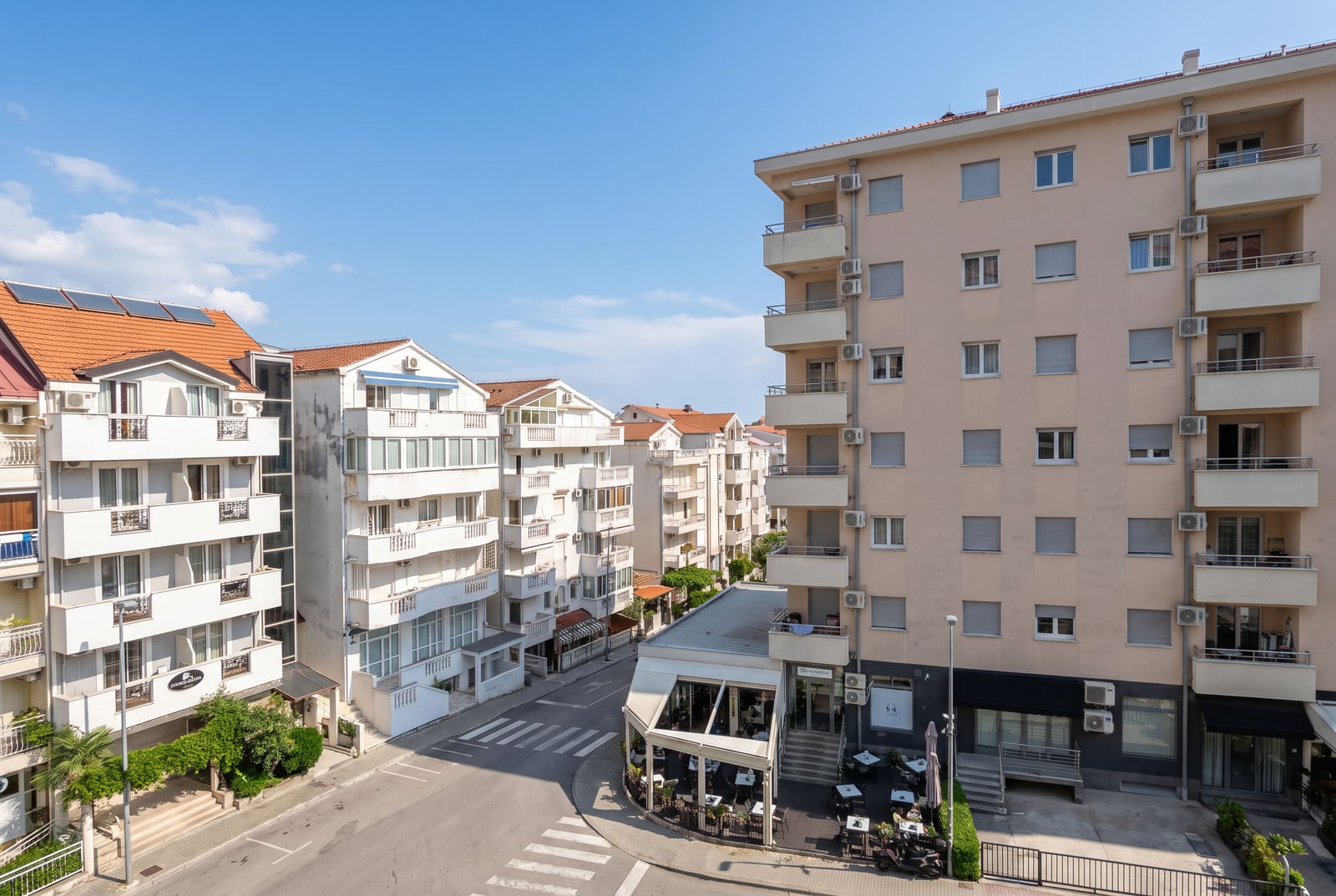 Street view of multi-story residential buildings, balconies, and an outdoor cafe area.